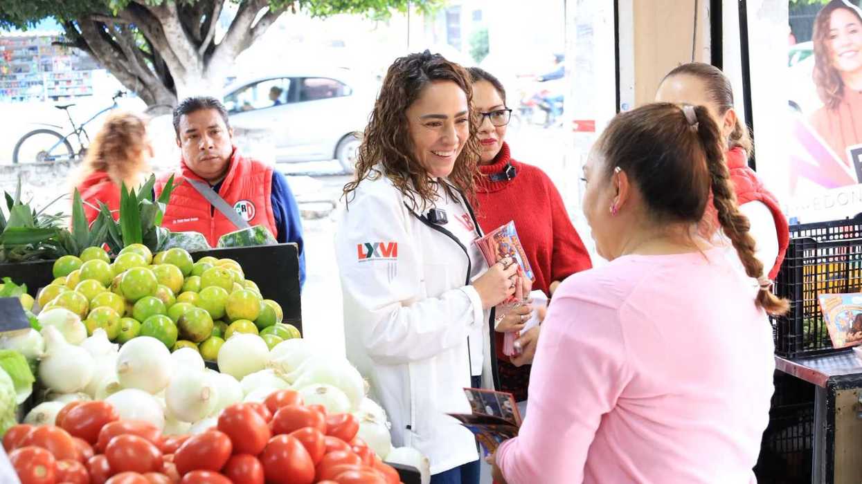 Abigail Arredondo Ramos entrega un volante a una comerciante en un puesto de verduras durante su recorrido en San Juan del Río