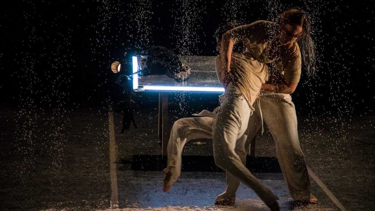 Actriz y actor caracterizados en una escena de teatro con vestuario colorido y máscaras de nariz prolongada.