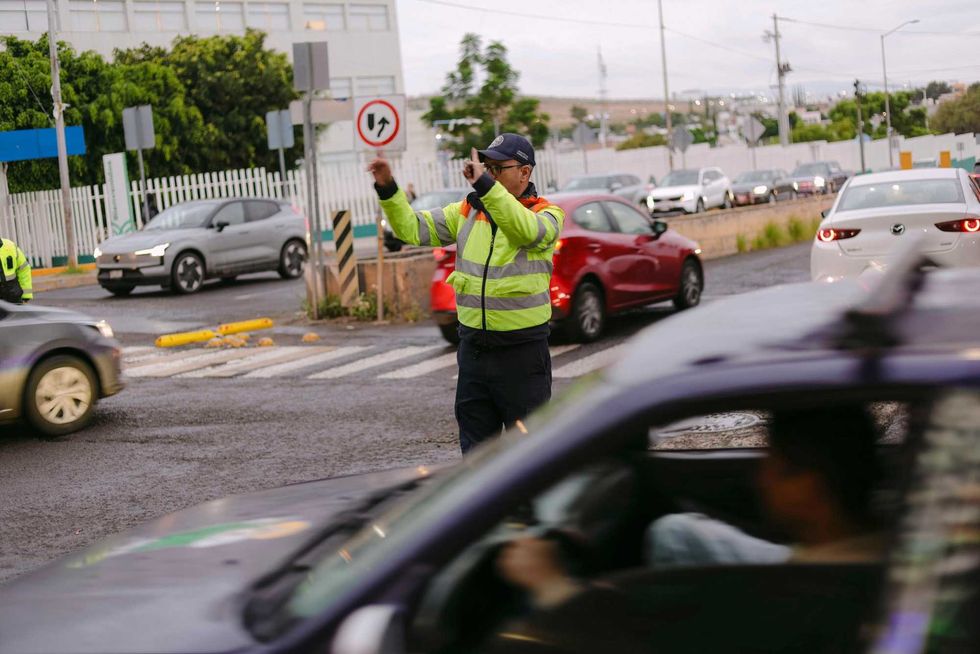 Agente de Movilidad de Corregidora, de espaldas, indica el paso a un autom\u00f3vil blanco durante el operativo vial