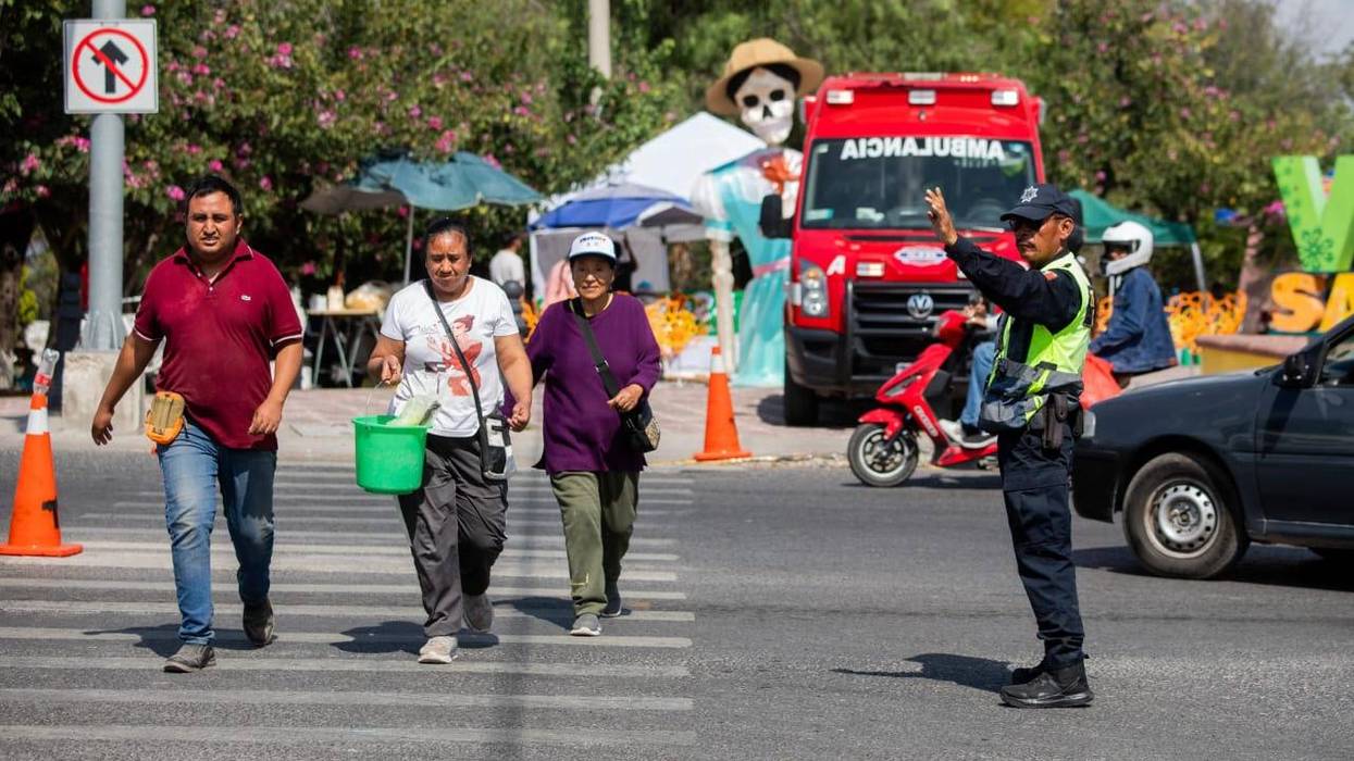 Agente indica el paso a tres peatones en el operativo de Día de Muertos en San Juan del Río, frente a una ambulancia