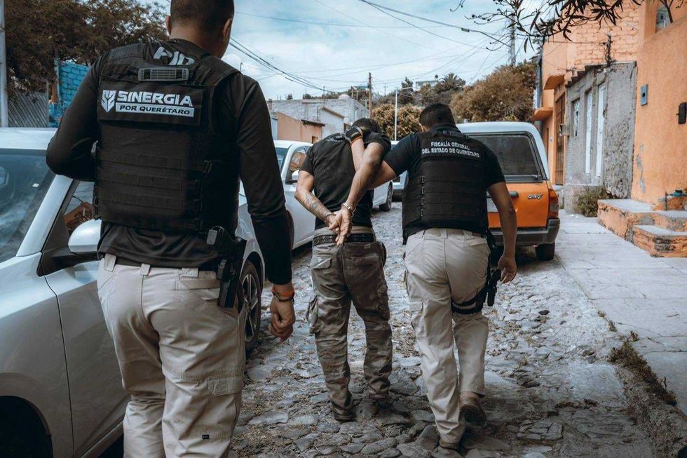 Agentes de la Fiscal\u00eda General y de Sinergia por Quer\u00e9taro trasladan esposado a un hombre detenido durante los cateos en la capital