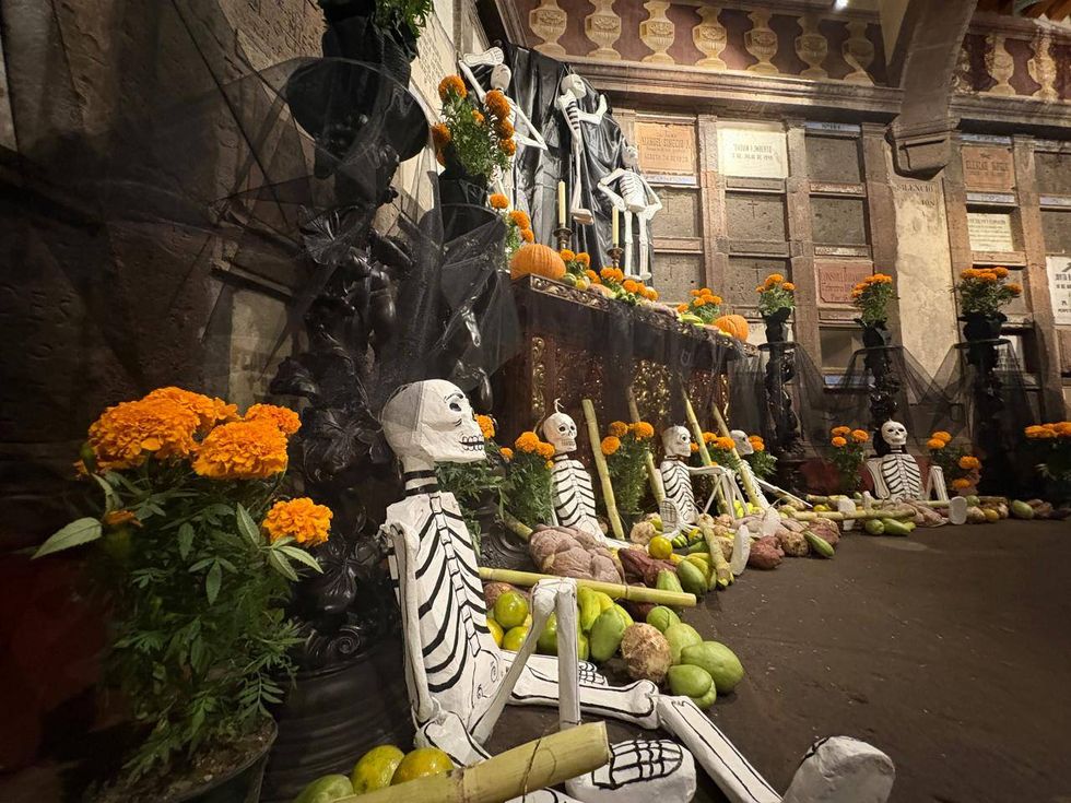 Altar de muertos con figuras de esqueletos, cempas\u00fachil, pan y fruta ante nichos del Museo de la Muerte de San Juan del R\u00edo
