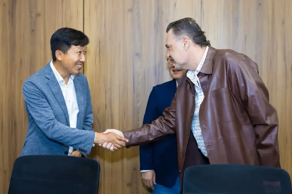 Apret\u00f3n de manos entre directivo de LS Cable y el gobernador Mauricio Kuri Gonz\u00e1lez en sala de reuni\u00f3n con paneles de madera al fondo