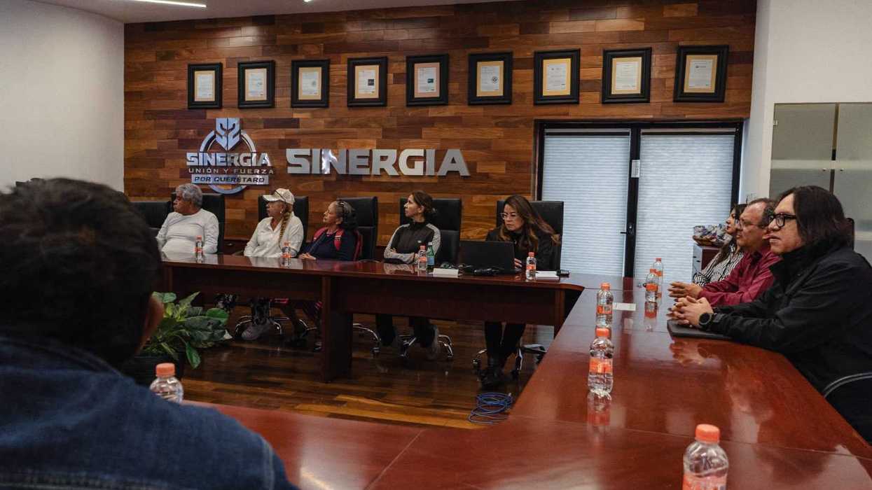 Asistentes a la mesa de trabajo de seguimiento con personas afectadas por fraude, sentados a una mesa de juntas frente a un muro con el logotipo de Sinergia.