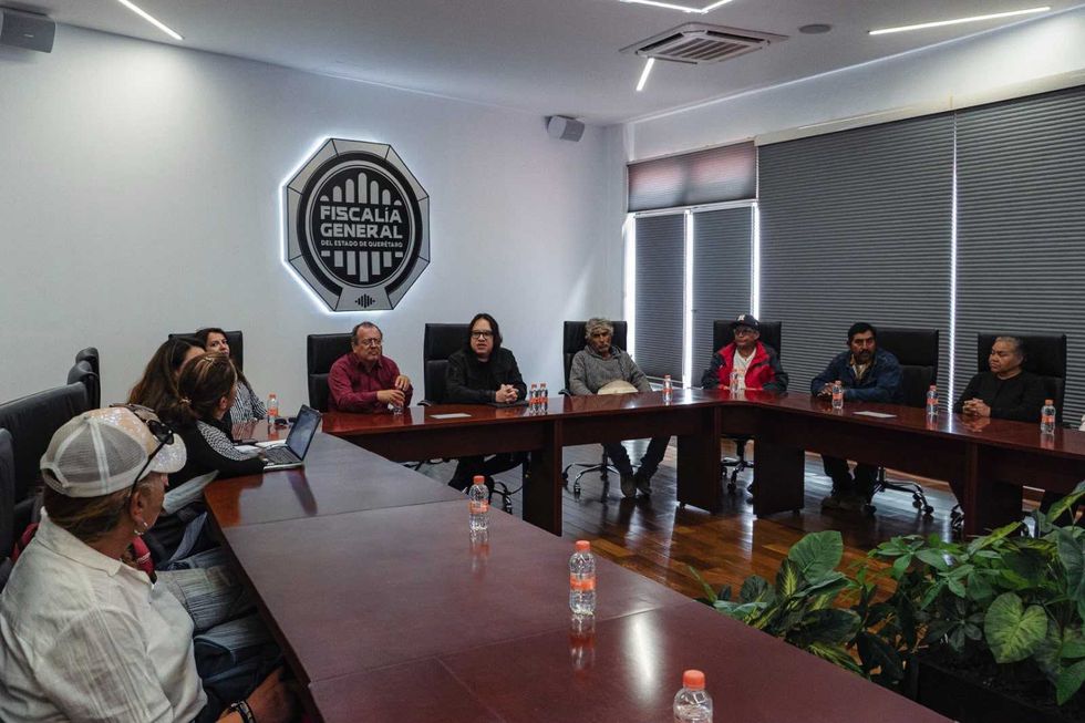 Asistentes a la mesa de trabajo de seguimiento con personas afectadas por fraude, sentados a una mesa de juntas frente a un muro con el logotipo de Sinergia.
