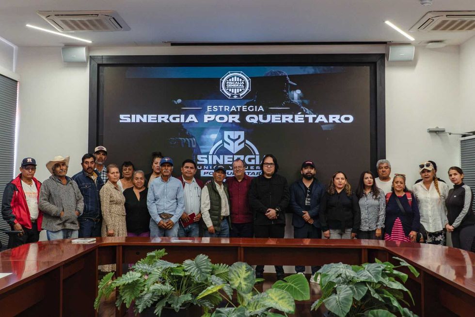 Asistentes a la mesa de trabajo de seguimiento con personas afectadas por fraude, sentados a una mesa de juntas frente a un muro con el logotipo de Sinergia.