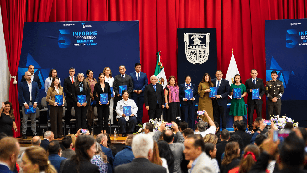 Asistentes a la sesi\u00f3n solemne sostienen ejemplares del quinto informe de gobierno de San Juan del R\u00edo sobre el escenario del Cabildo
