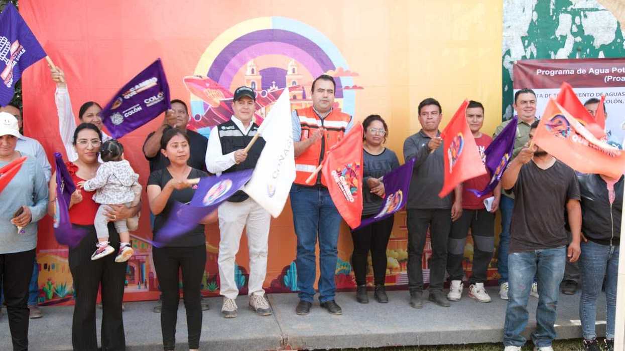 Asistentes al arranque de la planta de tratamiento de aguas residuales de El Blanco, en Colón, sostienen banderas frente a una lona del gobierno municipal.
