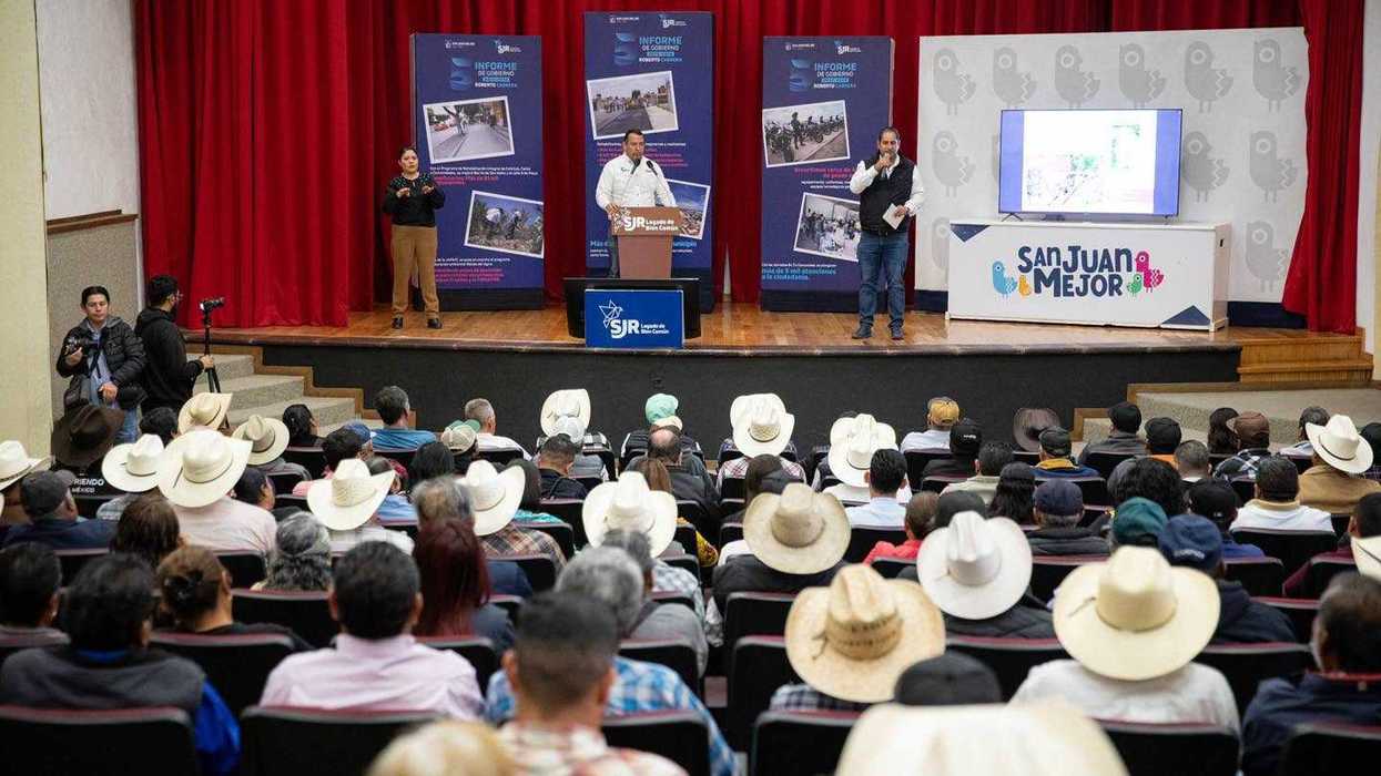 Asistentes con sombreros llenan un auditorio en el encuentro del alcalde de San Juan del Río con comisariados ejidales, con mantas del quinto informe al fondo del escenario.