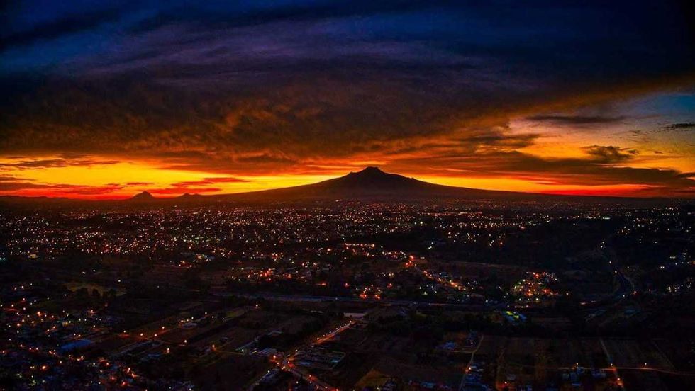 Atardecer sobre la ciudad de Tlaxcala con un volc\u00e1n al fondo y las luces de las calles encendidas, a 501 a\u00f1os de su fundaci\u00f3n