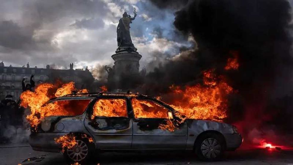 Autom\u00f3vil en llamas junto a una estatua entre columnas de humo negro durante los disturbios en Francia