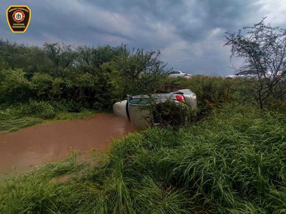 Autom\u00f3vil sed\u00e1n de color claro fuera de la vialidad, sobre una zona con vegetaci\u00f3n junto a un canal, a la altura de la carretera 200.