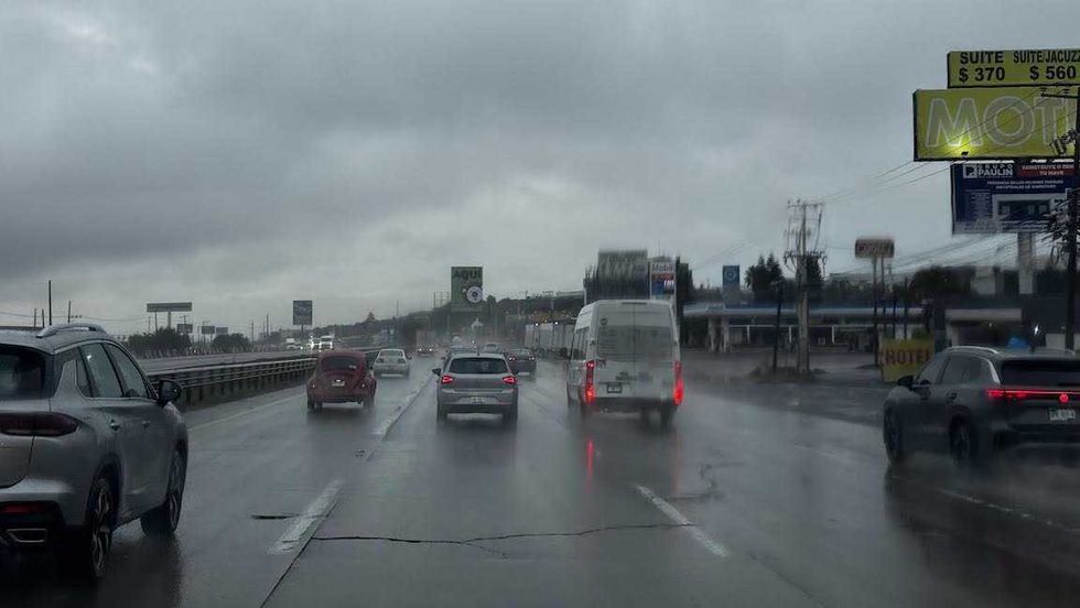 Autom\u00f3viles avanzan lentamente sobre una avenida con agua acumulada bajo cielo nublado en Quer\u00e9taro.