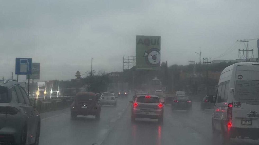Autom\u00f3viles avanzan lentamente sobre una avenida con agua acumulada bajo cielo nublado en Quer\u00e9taro.