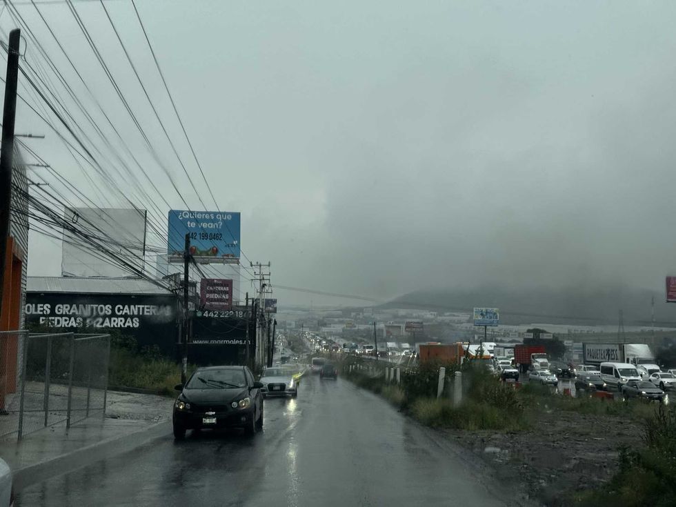 Autom\u00f3viles sobre pavimento mojado bajo la lluvia y cables el\u00e9ctricos en una vialidad de Quer\u00e9taro.