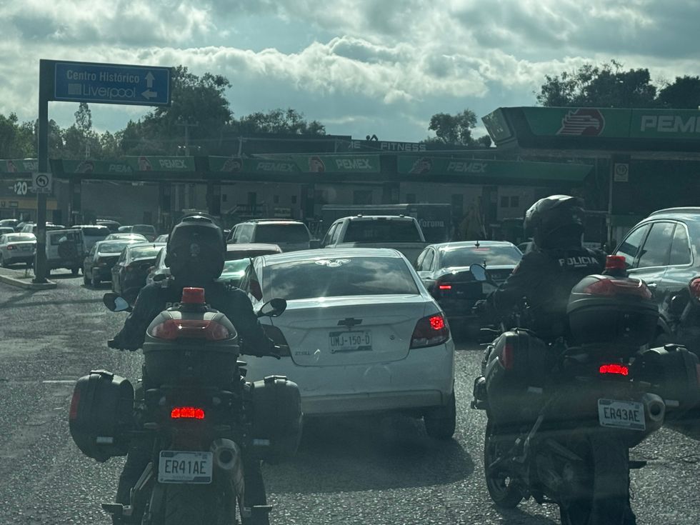 Autom\u00f3viles y motocicletas policiacas detenidas en una avenida saturada de San Juan del R\u00edo, con se\u00f1alamientos hacia el Centro Hist\u00f3rico y Amealco, y una gasolinera Pemex al fondo.