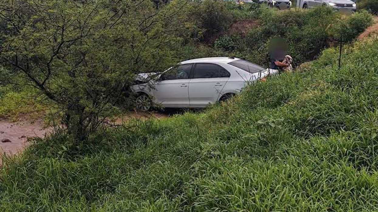 Automóvil sedán de color claro fuera de la vialidad, sobre una zona con vegetación junto a un canal, a la altura de la carretera 200.
