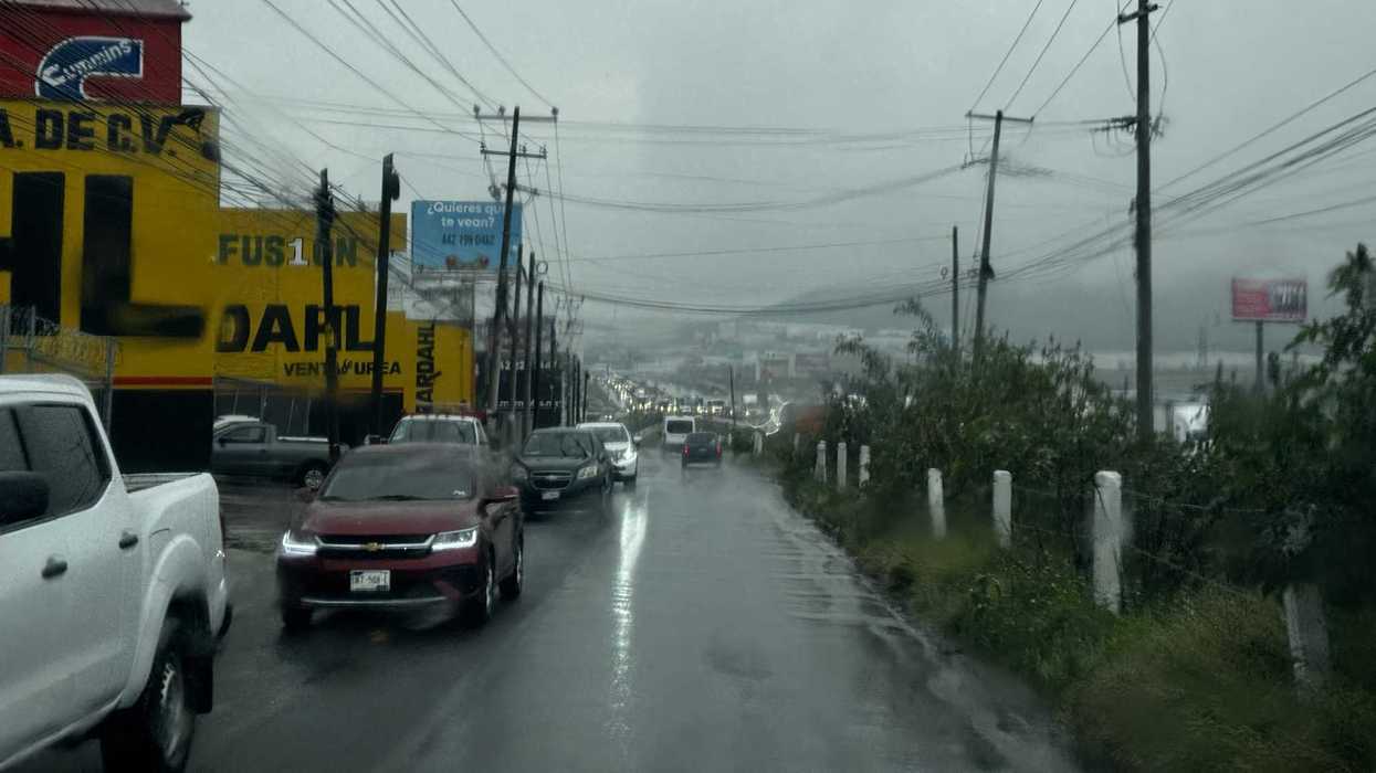 Automóviles sobre pavimento mojado bajo la lluvia y cables eléctricos en una vialidad de Querétaro.
