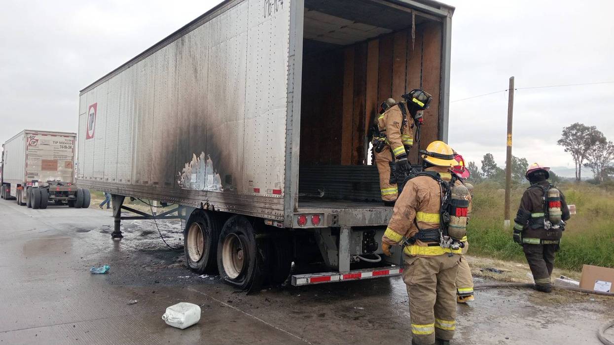 Bomberos con equipo de respiración autónoma junto a la caja abierta de un tráiler con huellas de fuego en San Juan del Río