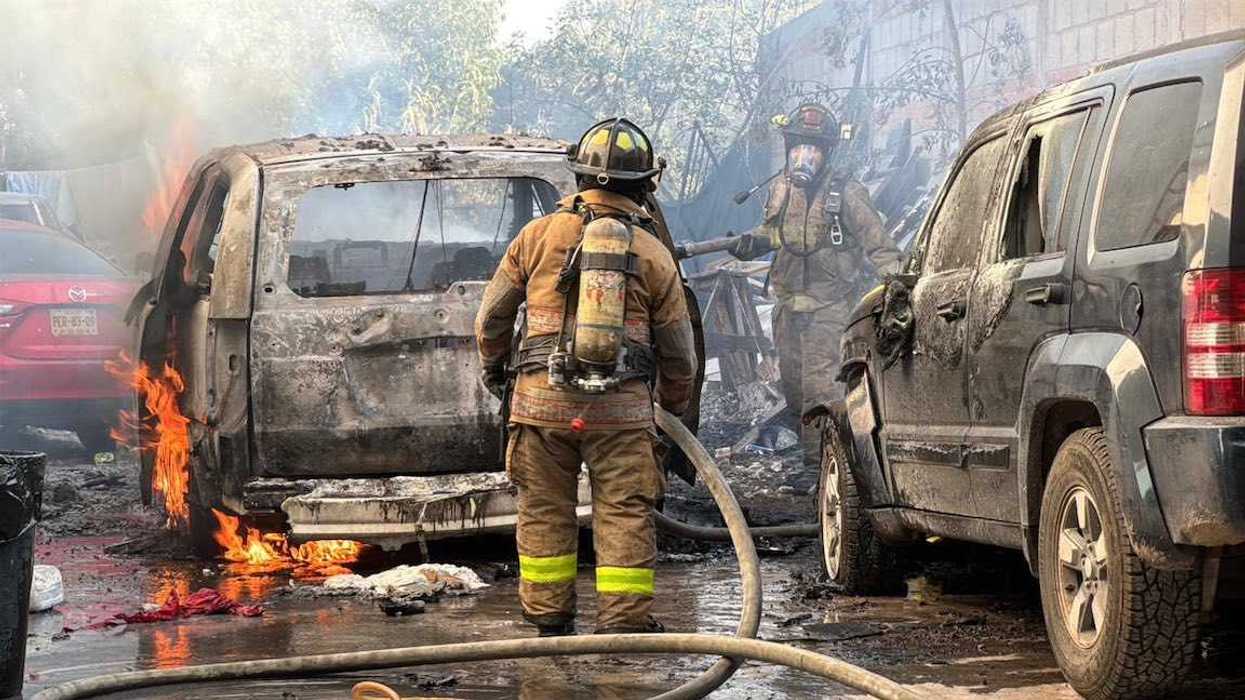 Bomberos de San Juan del Río controlan el fuego junto a dos vehículos calcinados en el patio de un domicilio.
