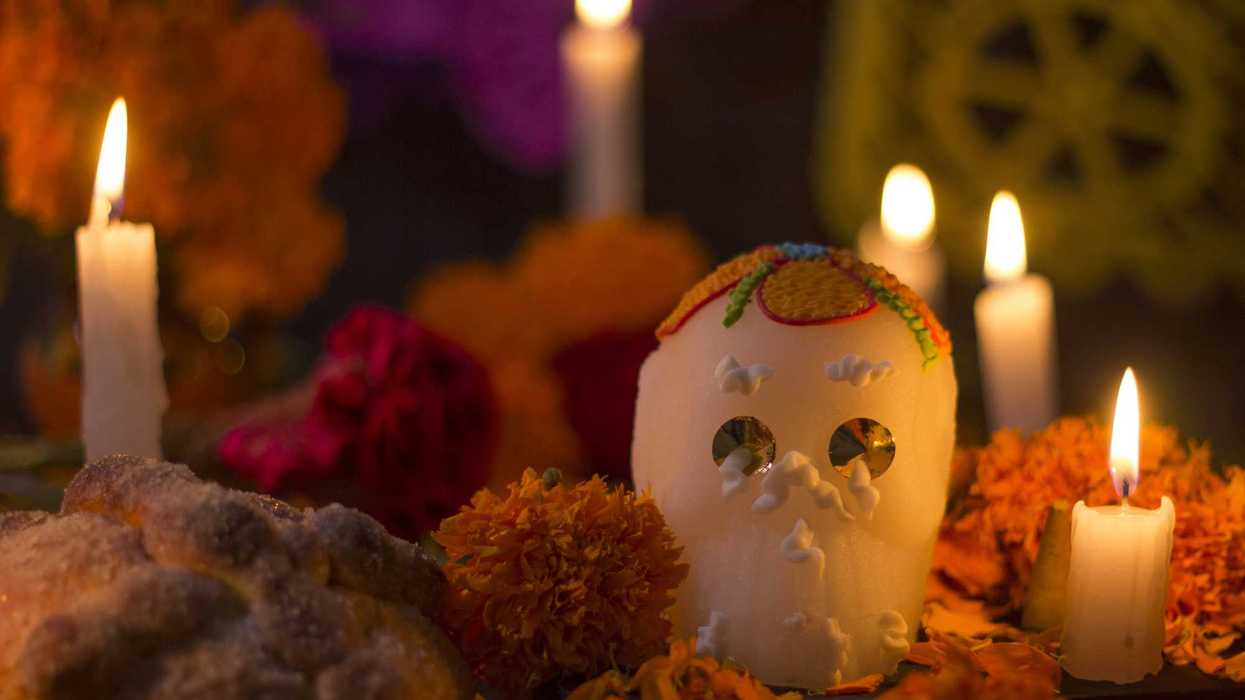 Calavera de azúcar rodeada de veladoras encendidas, flores de cempasúchil y pan de muerto en una ofrenda de Día de Muertos