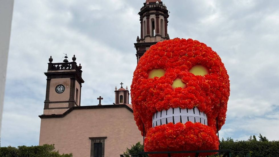 Calavera monumental cubierta de flores naranjas frente a las torres de un templo en el centro de San Juan del R\u00edo
