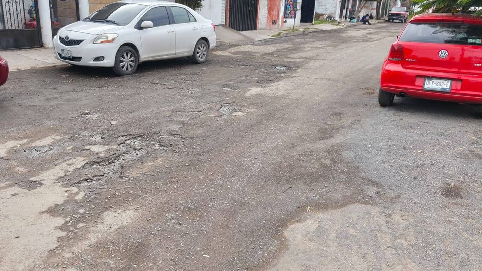 Calle de La Pe\u00f1a con asfalto desgastado y parchado, un sed\u00e1n blanco y un auto rojo estacionados a los lados
