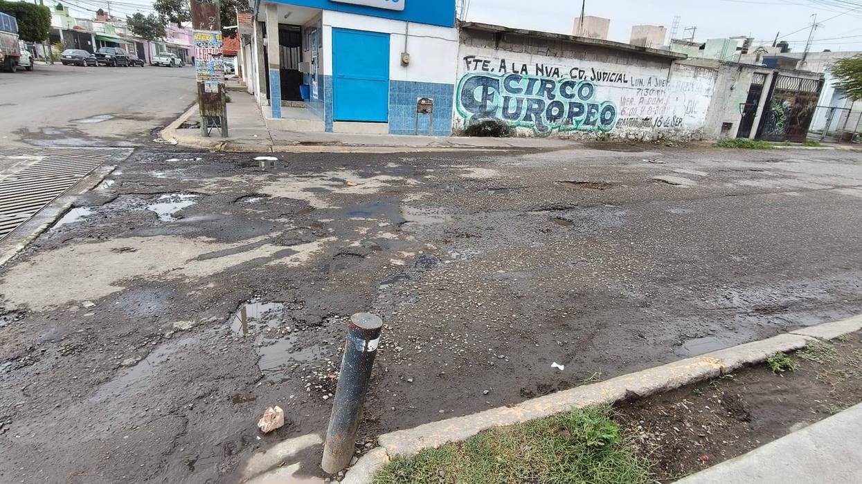 Calle de La Peña con grandes baches llenos de agua en el centro del carril y un auto oscuro a la derecha