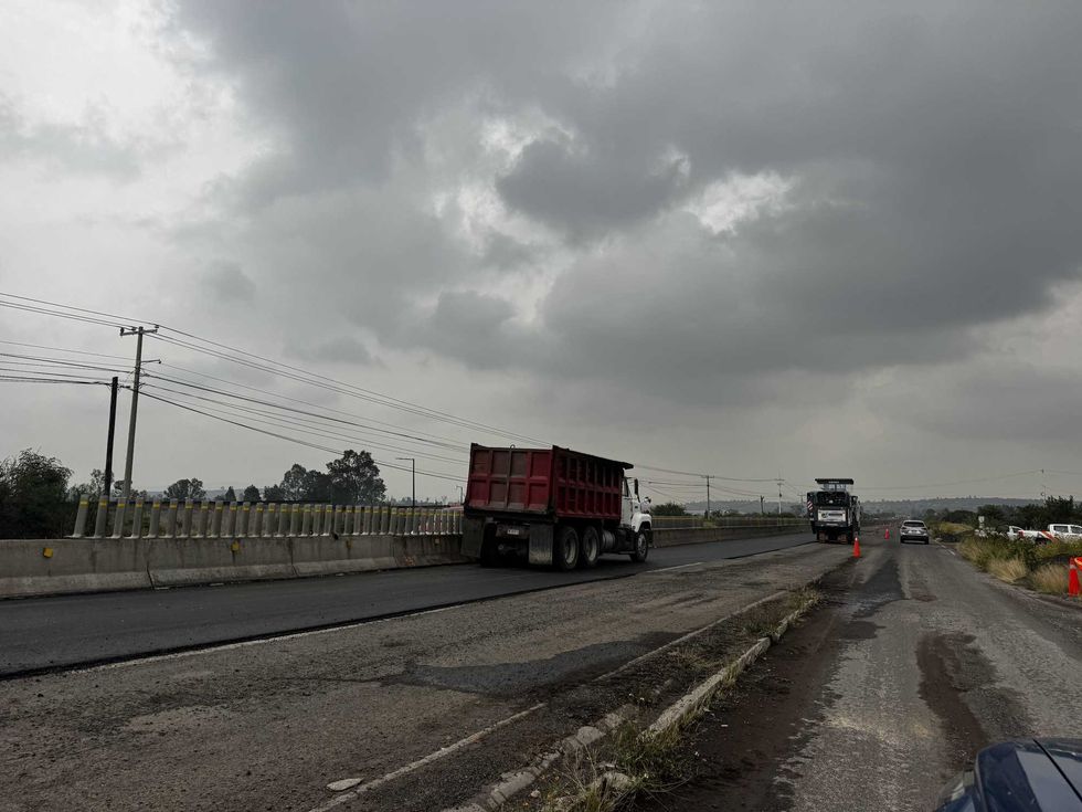 Cami\u00f3n de volteo sobre carril con asfalto nuevo y maquinaria de fresado en la