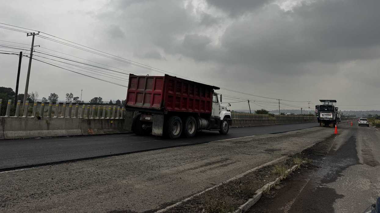 Camión de volteo sobre carril con asfalto nuevo y maquinaria de fresado en la
