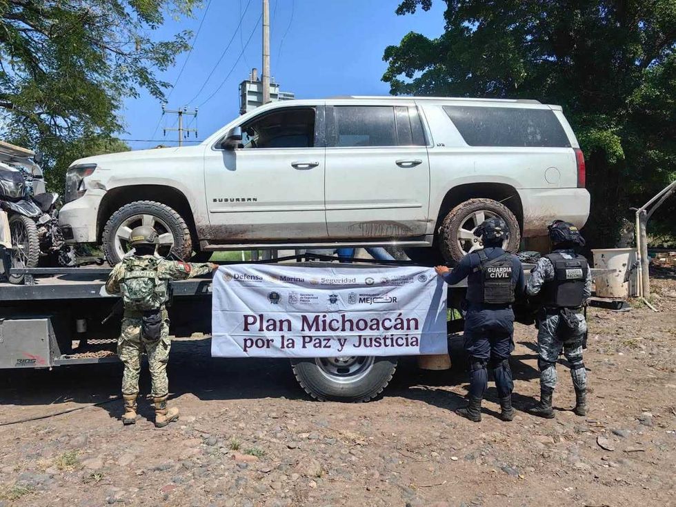 Camioneta tipo Suburban blanca sobre una gr\u00faa, con elementos militares y de la Guardia Civil sosteniendo una lona con el mensaje "Plan Michoac\u00e1n por la Paz y Justicia"
