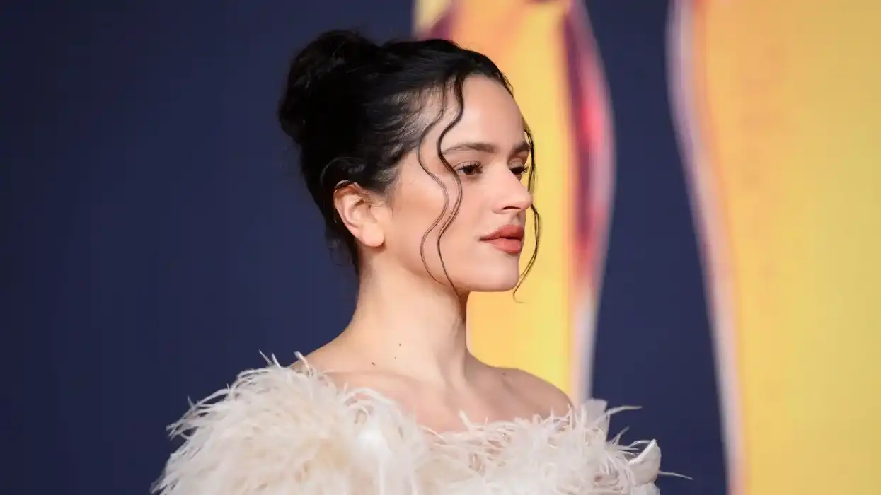 Cantante de perfil, con el cabello recogido y vestido de plumas blancas, ante un fondo azul marino y amarillo