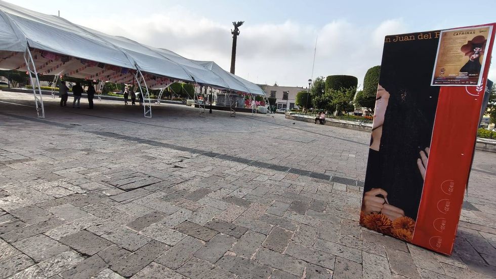 Carpa blanca del Festival de D\u00eda de Muertos y cartel del concurso de catrinas en una plaza de San Juan del R\u00edo