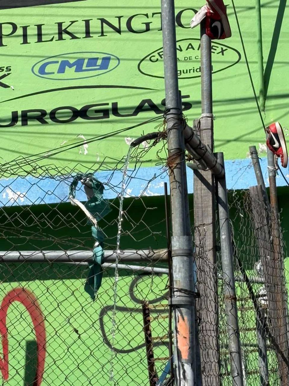 Chorro de agua sale de una manguera sujeta a un poste met\u00e1lico junto a una malla cicl\u00f3nica en avenida R\u00edo Moctezuma, San Juan del R\u00edo.