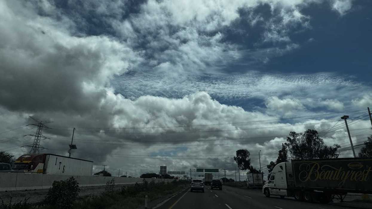 Cielo con nubes densas y claros azules sobre una autopista con tráfico de carga y vehículos particulares