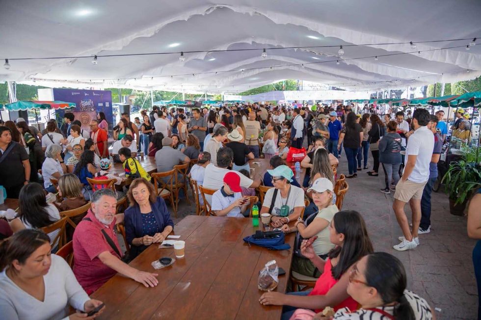 Cientos de asistentes en mesas largas y de pie bajo una carpa blanca durante el Festival del Caf\u00e9 en San Juan del R\u00edo.