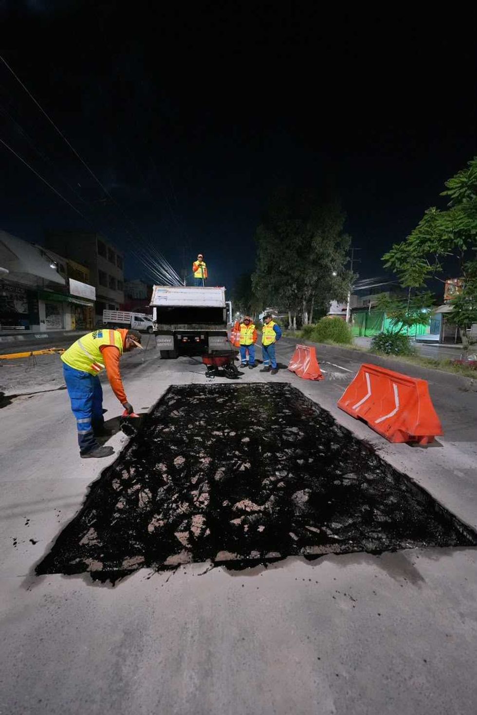 Cuadrilla municipal trabaja sobre bache con pala y pipa de asfalto al anochecer en Quer\u00e9taro