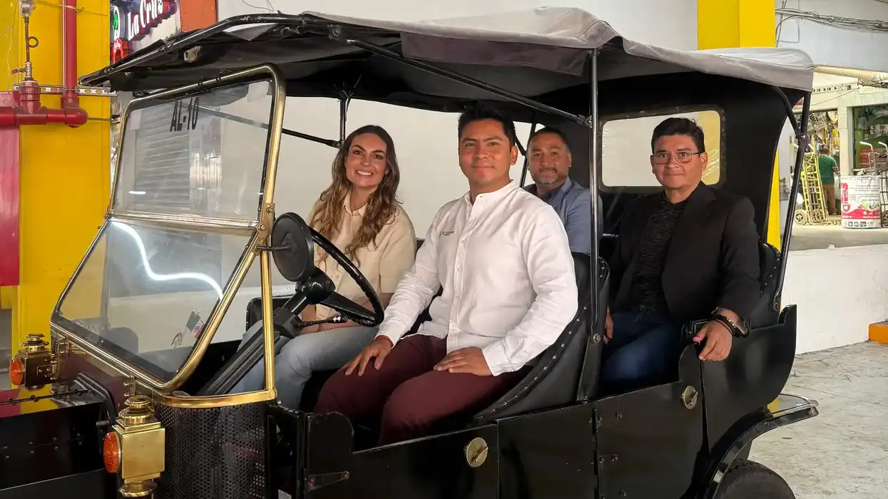 Cuatro personas a bordo de un vehículo tipo tranvía turístico antiguo en un espacio techado
