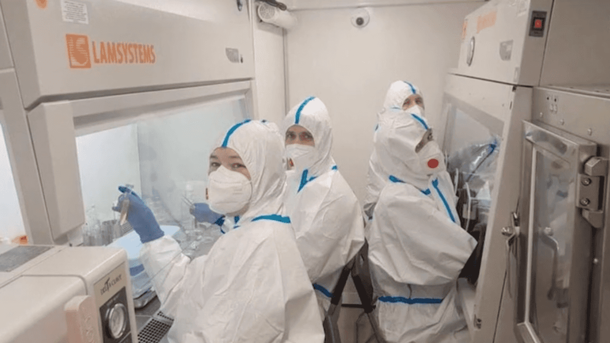 Cuatro personas con trajes de protección y cubrebocas trabajan en cabinas de bioseguridad de un laboratorio