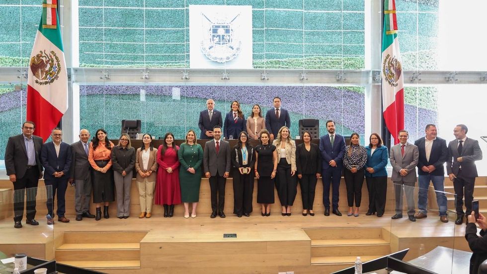 de veinte personas posan de pie en el recinto de la Legislatura de Quer\u00e9taro durante la Sesi\u00f3n Solemne de la Medalla de Honor Alejandra J\u00e1idar Matalobos, entre banderas de M\u00e9xico y un escudo.