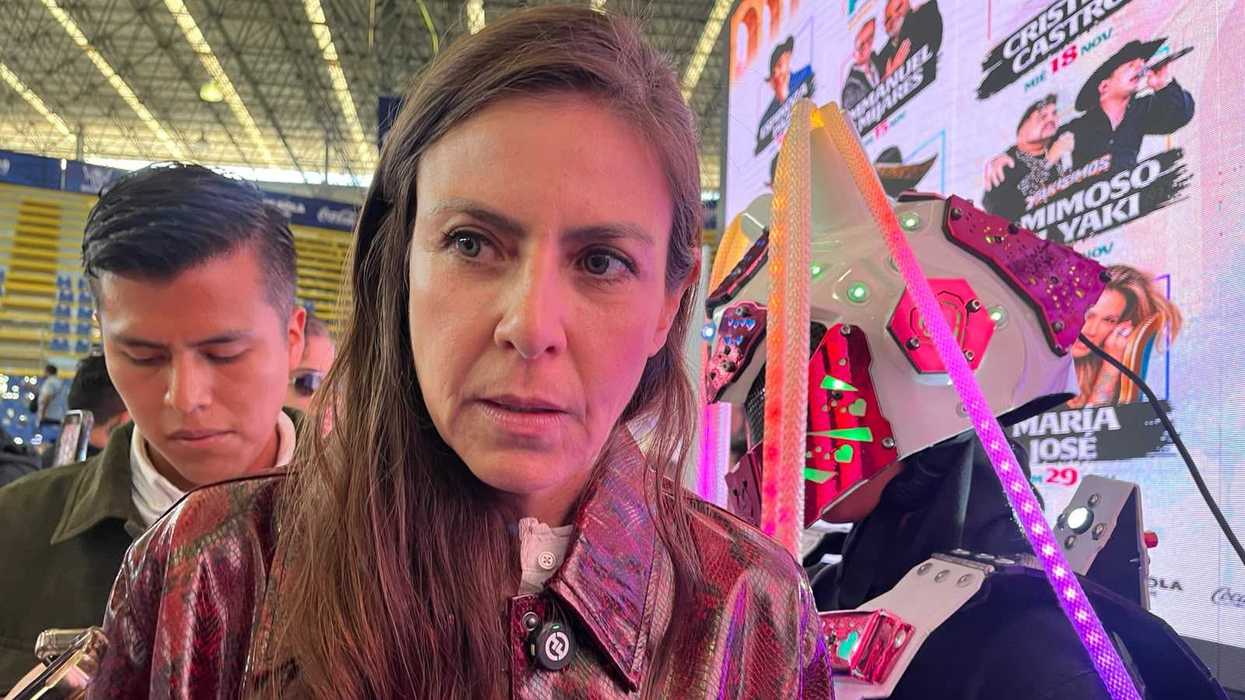 Declaraciones sobre la derrama económica por Día de Muertos en Querétaro: una funcionaria habla con reporteros ante una pantalla con carteles de conciertos