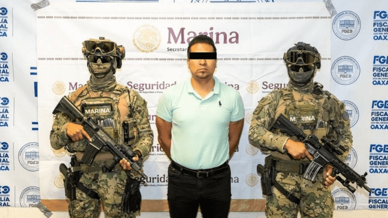 Detenido por extorsión en la Central de Abasto, Oaxaca, entre elementos de seguridad frente a una lona de la Fiscalía