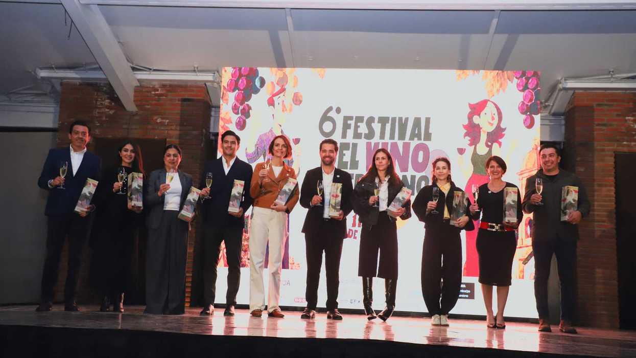 Diez personas levantan copas sobre un escenario frente a la pantalla del 6° Festival del Vino Queretano