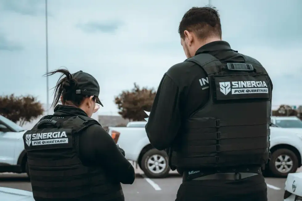 Dos agentes de espaldas con chalecos t\u00e1cticos de la estrategia Sinergia por Quer\u00e9taro durante un operativo.