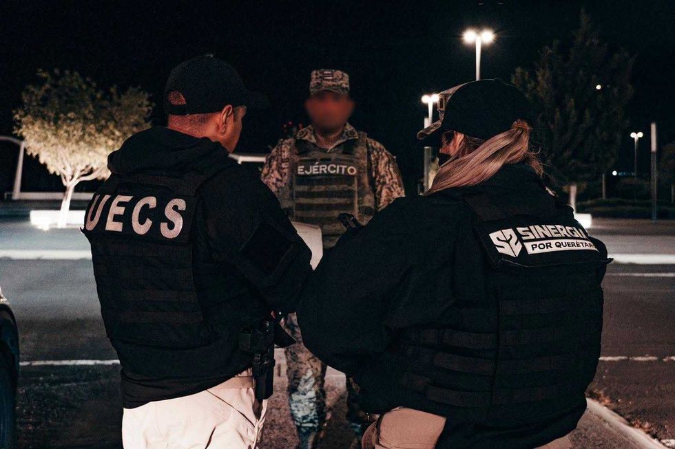 Dos agentes de espaldas, uno con chaleco de la Unidad Especializada de Combate al Secuestro (UECS) y otra con chaleco de "Sinergia por Quer\u00e9taro", frente a un elemento del Ej\u00e9rcito mexicano con el rostro difuminado, durante un operativo nocturno.
