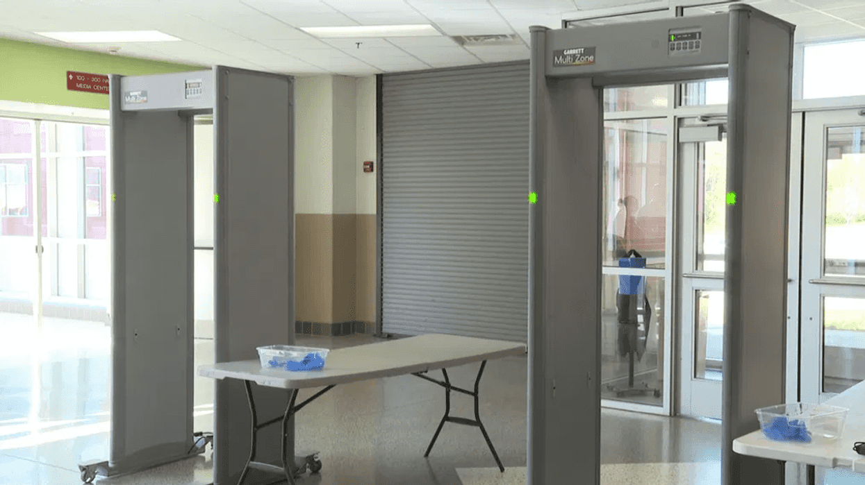 Dos arcos detectores de metales y una mesa plegable con guantes azules en un vestíbulo con puertas de cristal