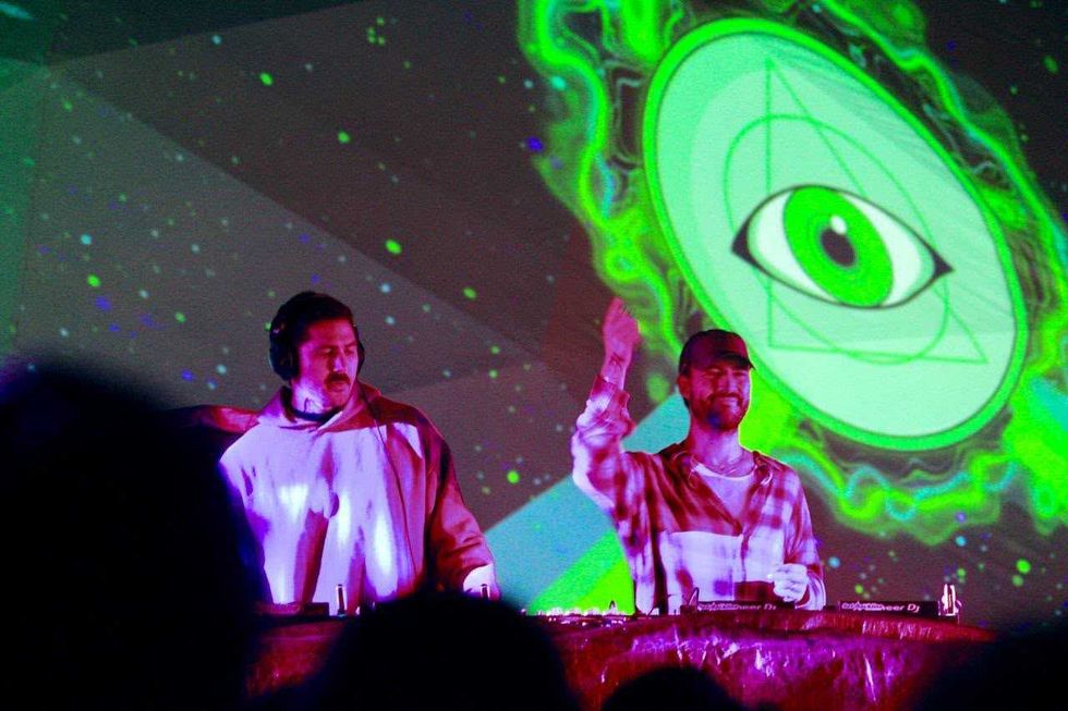 Dos DJ frente a una proyecci\u00f3n verde con un ojo, durante la programaci\u00f3n musical de INVERSA 2026 en Plaza Fundadores