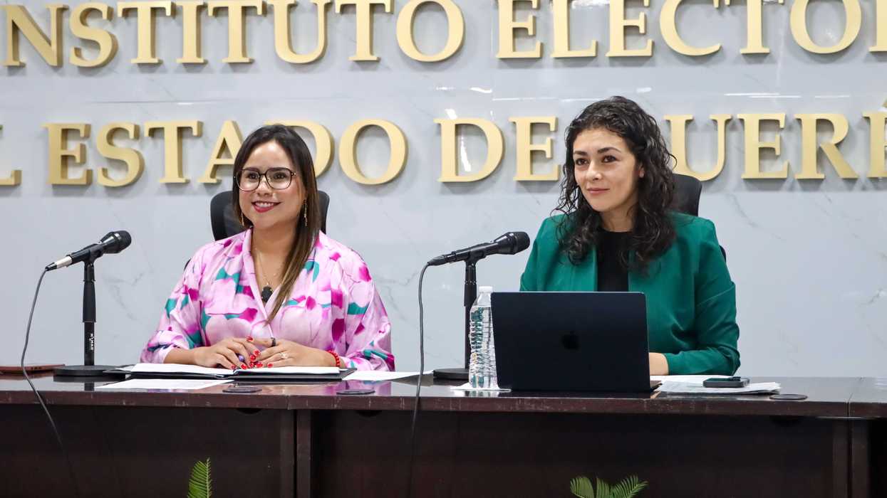 Dos funcionarias del IEEQ presiden la sesión del Consejo General ante el logotipo institucional, en Querétaro.