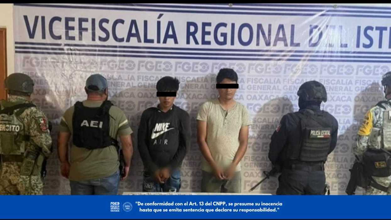 Dos hombres con los ojos cubiertos, junto a personal del Ejército, la AEI, la Policía Estatal y la Guardia Nacional, frente a la lona de la Vicefiscalía Regional del Istmo de la FGEO por el caso de extorsión en Juchitán, Oaxaca.