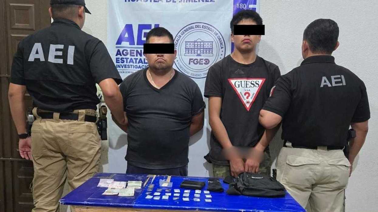 Dos hombres detenidos por la AEI, rostros cubiertos, junto a mesa con dinero asegurado en Huautla de Jiménez